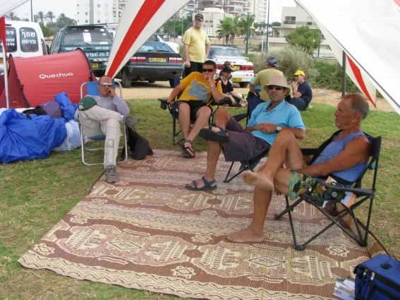טייסים ונוסעים יושבים בצל אוהל על שטיחים בשדה ההמראה, בין טיסה לטיסה