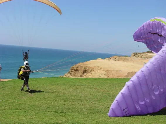 טייס ממריא מהדשא בראש המצוק, כנף סגולה בחזית והים מאחור