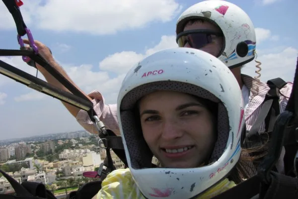 נוסעת מחייכת בקסדה לבנה באוויר, המדריך מאחוריה והעיר למטה